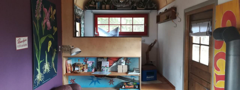 benno der wagen aussergewoehnliche unterkunft zirkuswagen schiessbude tiny house weniger ist mehr es braucht nicht viel zum gluecklichsein frankenwald rennsteig nordbayern bayern ganz weit oben thueringen recycle reuse upcycling second hand flohmarktfunde kleinanzeigen wiederverwenden urlaub im gruenen in der natur ruhe waldbaden innenaufnahme sessel eingang bett