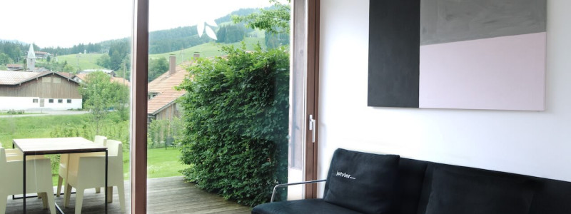jotvier jungholz ferienwohnung allgäu urlaub in den bergen in der natur mit der familie mit hund nachhaltige bauweise heimische natürliche hölzer baumaterialien wohnraum dunkles sofa blick auf terrasse