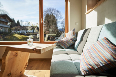 stadtalm toelzer land bad toelz urlaub in deutschland in der natur in bayern in den bergen auf dem land im gruenen nachhaltige oekologische unterkunft holz lehm bienen lamas kubische bauweise alpinarchitektur sofa wohnraum blick nach draussen garten