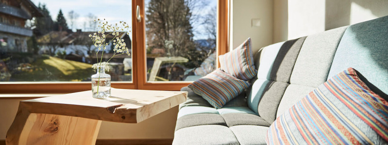 stadtalm toelzer land bad toelz urlaub in deutschland in der natur in bayern in den bergen auf dem land im gruenen nachhaltige oekologische unterkunft holz lehm bienen lamas kubische bauweise alpinarchitektur sofa wohnraum blick nach draussen garten
