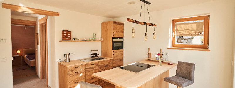 stadtalm toelzer land bad toelz urlaub in deutschland voralpenland in der natur in bayern in den bergen auf dem land im gruenen nachhaltige oekologische unterkunft holz lehm bienen lamas kubische bauweise alpinarchitektur ferienwohnung alpakaglueck kueche bar blick ins schlafzimmer